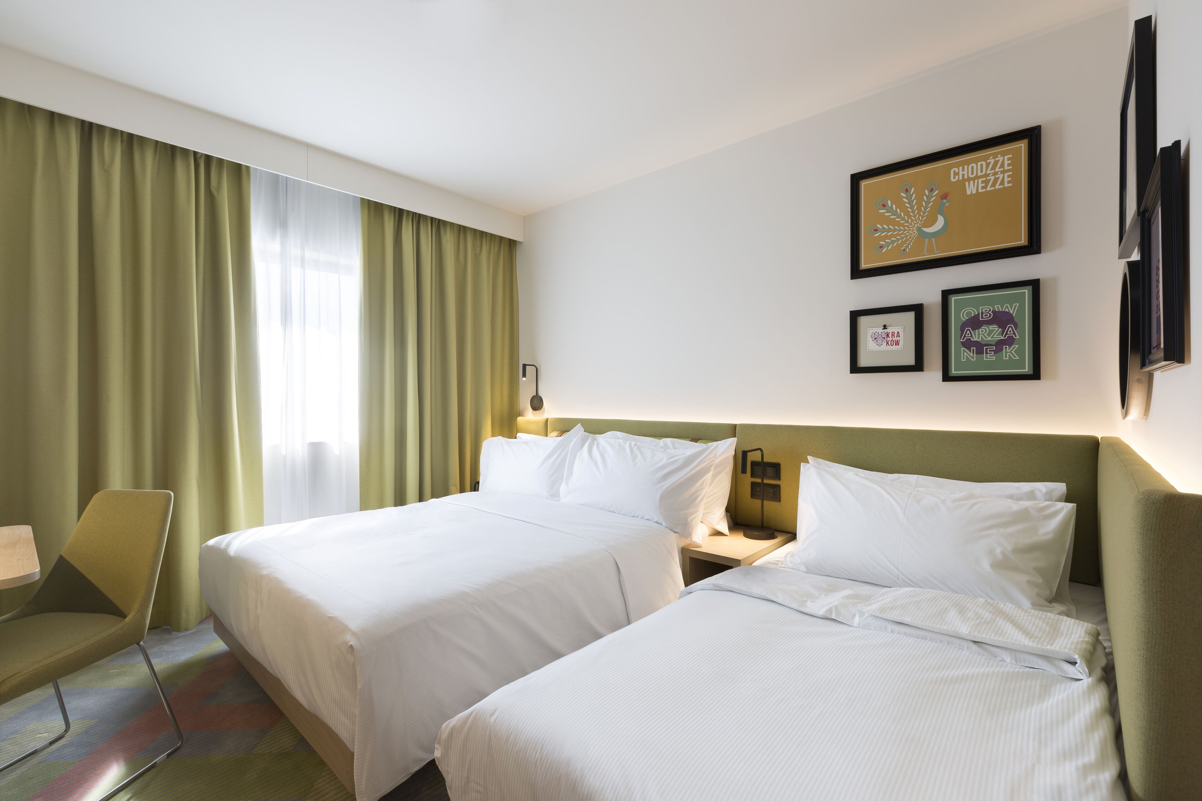 A hotel room with two beds, a chair, a desk, and a window with curtains.