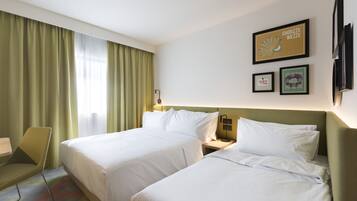 A hotel room with two beds, a chair, a desk, and a window with curtains.
