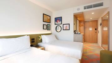 A hotel room with two beds, a nightstand, a mirror, and a wall with framed pictures.