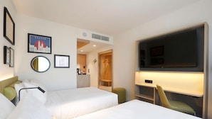 A hotel room with two beds, a TV, a desk, and a mirror.