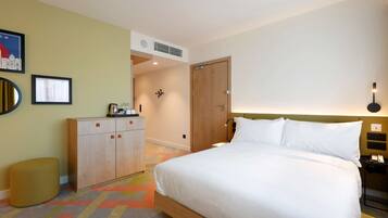 A hotel room with a bed, a wardrobe, a small stool, a nightstand, and a wall-mounted lamp.