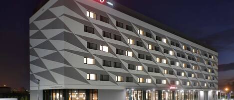 Un hotel moderno con fachada geométrica, varios pisos y un llamativo letrero de 'Hampton'.