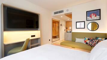 Una habitación de hotel moderna con una cama grande, un escritorio con una silla, un televisor, un sofá y un espejo.