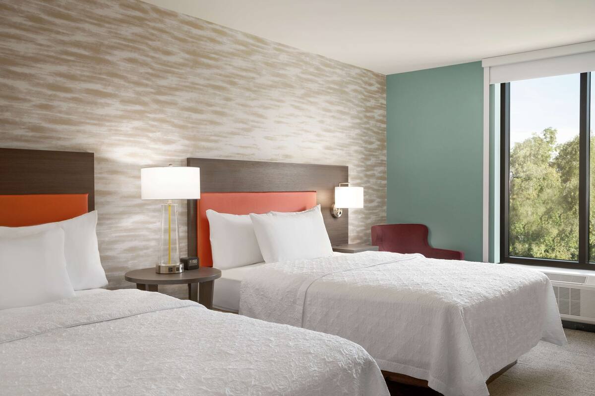 Habitación de hotel con dos camas, un ventanal grande y vistas a árboles.