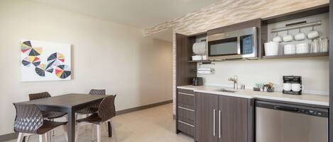 A modern kitchen with a dining area, featuring a microwave, coffee maker, and cabinets.