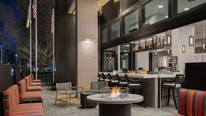 Un área de estar al aire libre con una mesa redonda y sillas, una zona de bar con mostrador y taburetes, y vistas de la ciudad iluminada de noche.