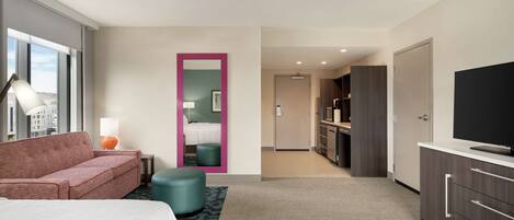 A hotel room with a bed, a sofa, a TV, a desk, and a bathroom visible through a door.