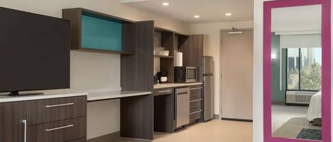 Habitación de hotel moderna con televisor de pantalla plana, kitchenette, espejo grande y vistas al exterior.
