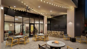 Un área de patio al aire libre con varias mesas y sillas, un brasero, luces colgantes y un ventilador de techo.