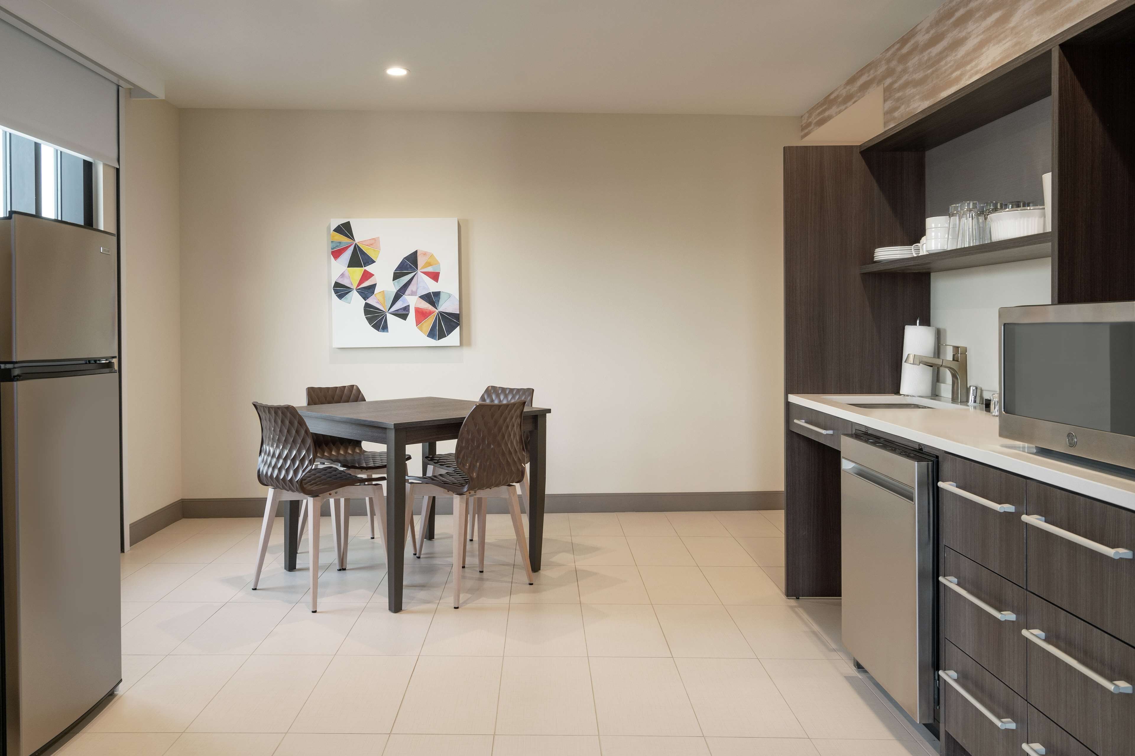 A modern kitchen with a dining table, chairs, a refrigerator, and a built-in oven.
