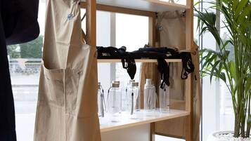 A shelf with various items including a beige apron, black bags, glass bottles, ceramic mugs, and a potted plant.