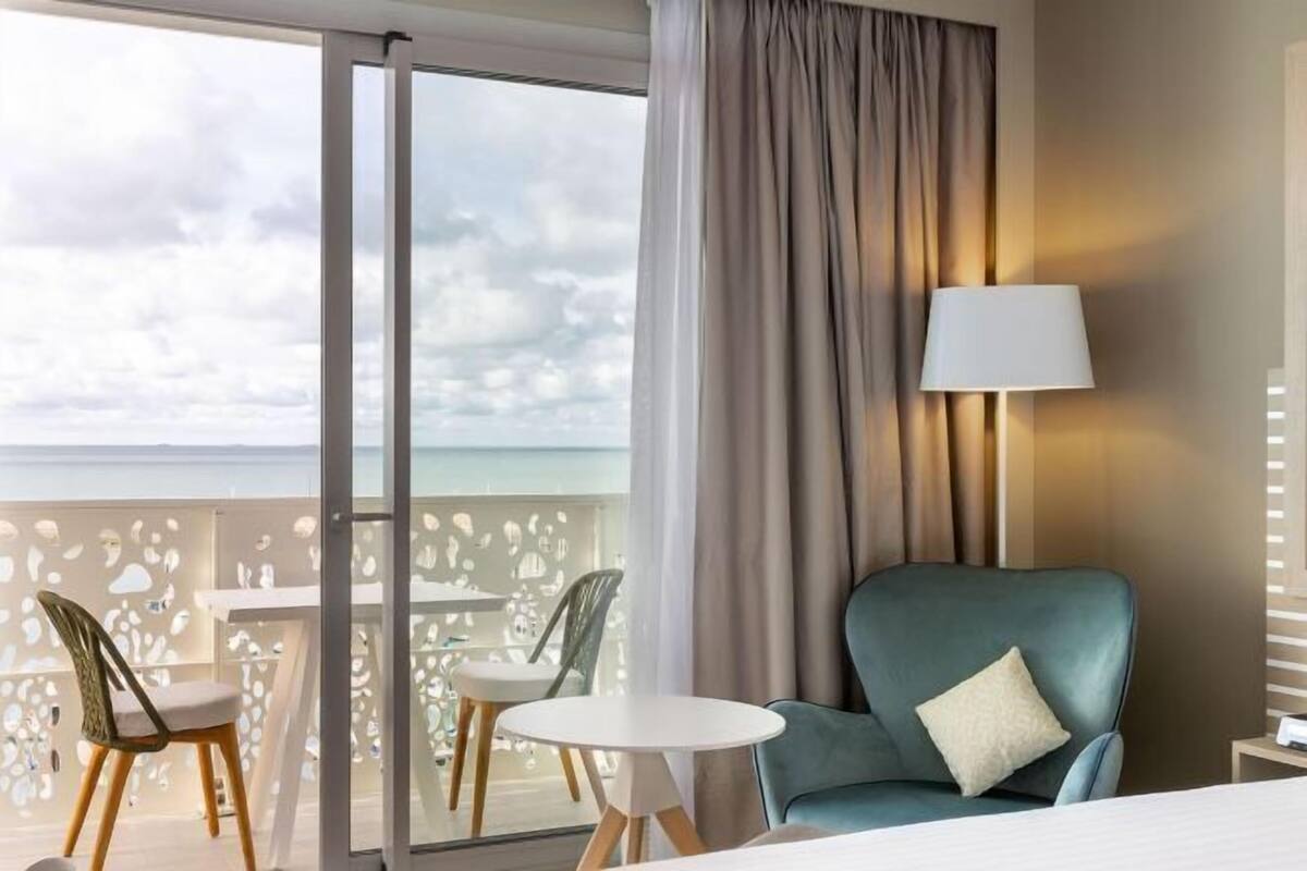 Une chambre d’hôtel avec un balcon, un canapé, une table et des chaises.