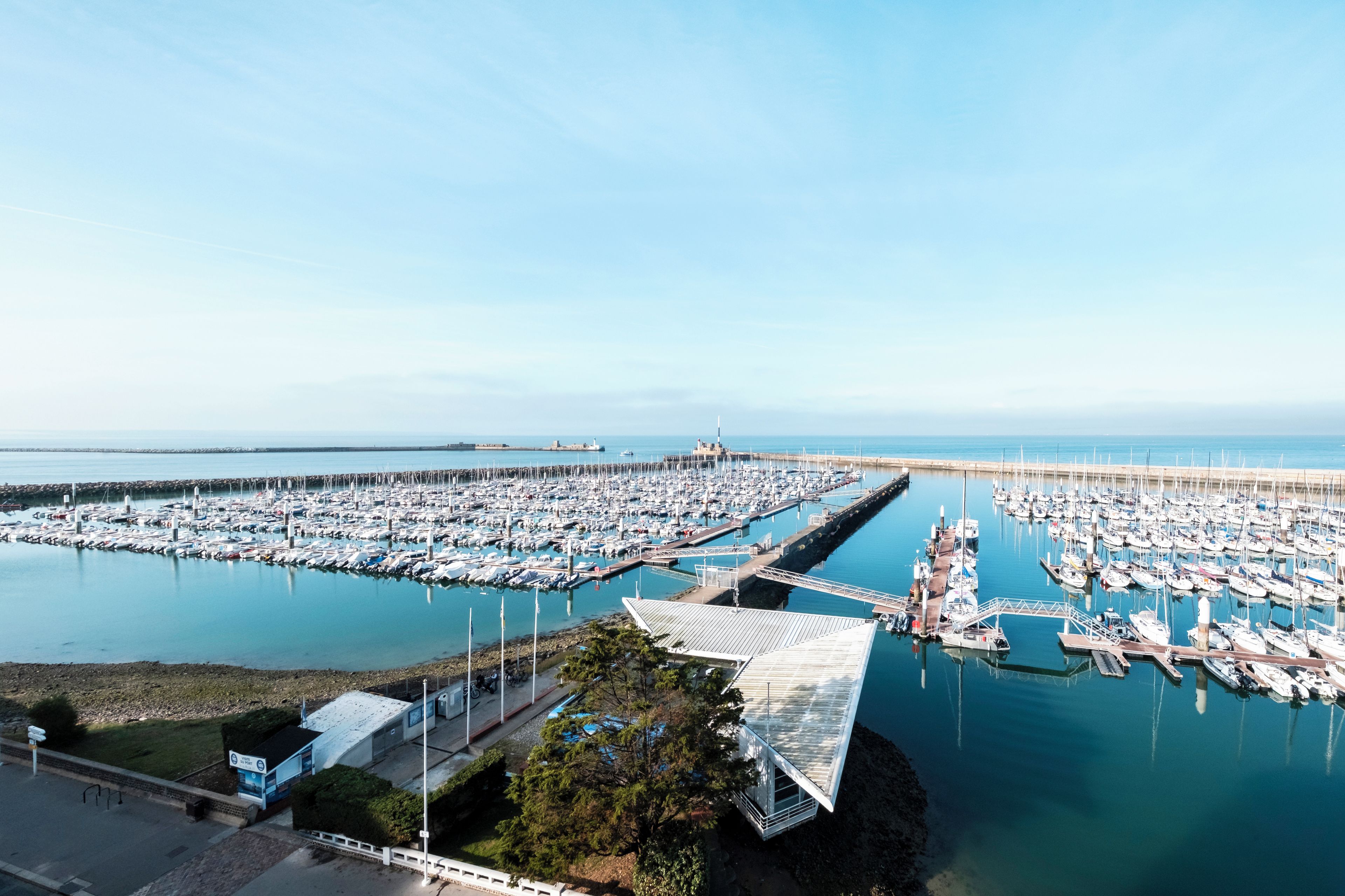 A marina with numerous boats docked, a clear sky, and a distant lighthouse.