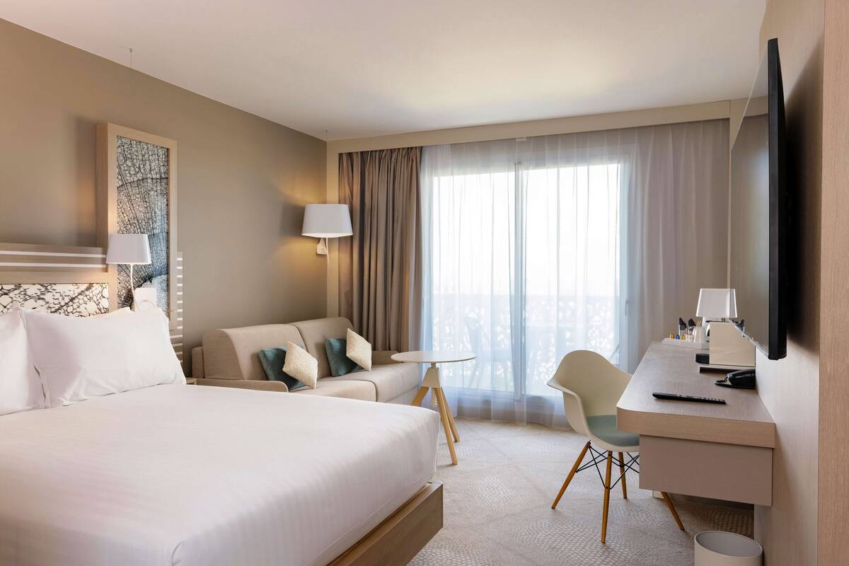 Une chambre d’hôtel avec un grand lit, un bureau avec une chaise, une petite table et un téléviseur.