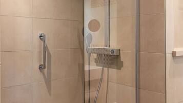 A glass-enclosed shower with a handheld showerhead and a wall-mounted control panel.