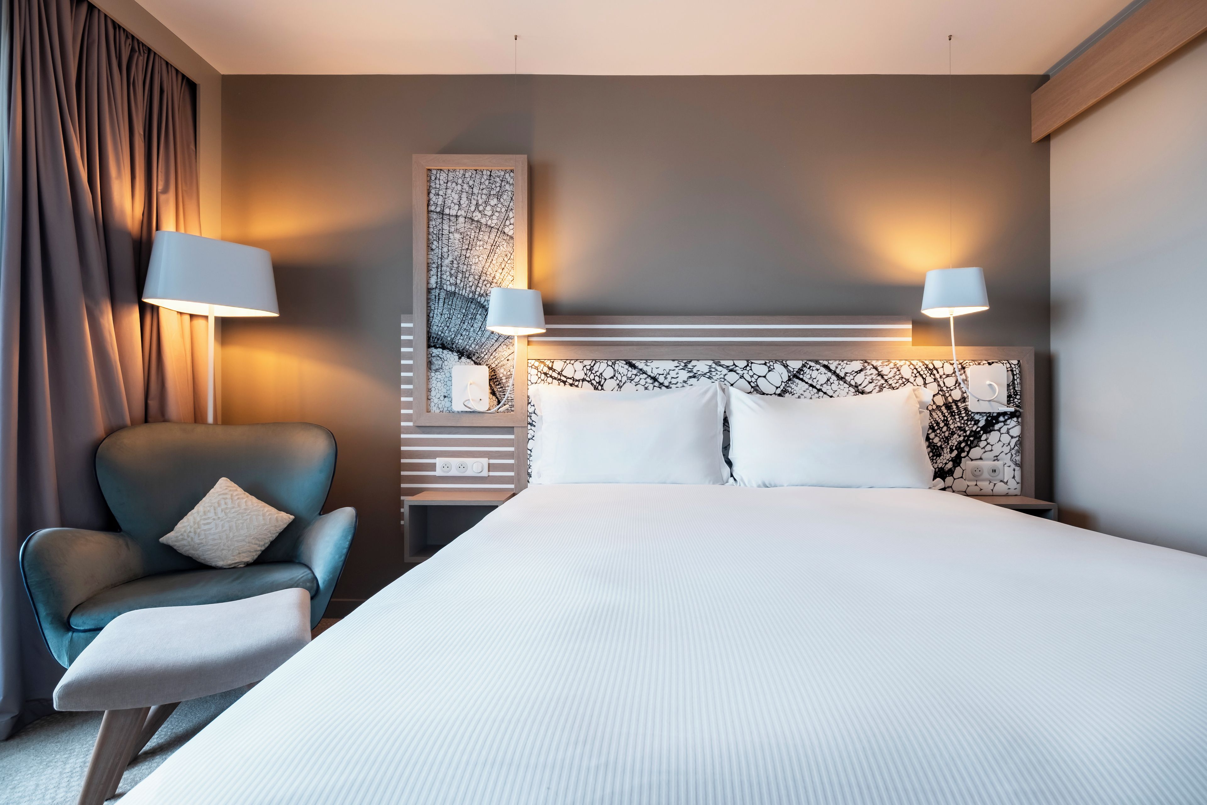 A hotel room with a large bed, two bedside lamps, a chair, and a wall-mounted artwork.