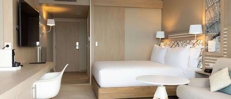 A modern hotel room with a bed, a desk, a chair, a sofa, and a TV.