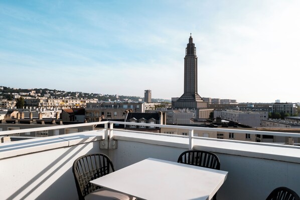 Een terras op het dak, met een tafel en stoelen, met uitzicht op een stadsbeeld en een opvallende toren.
