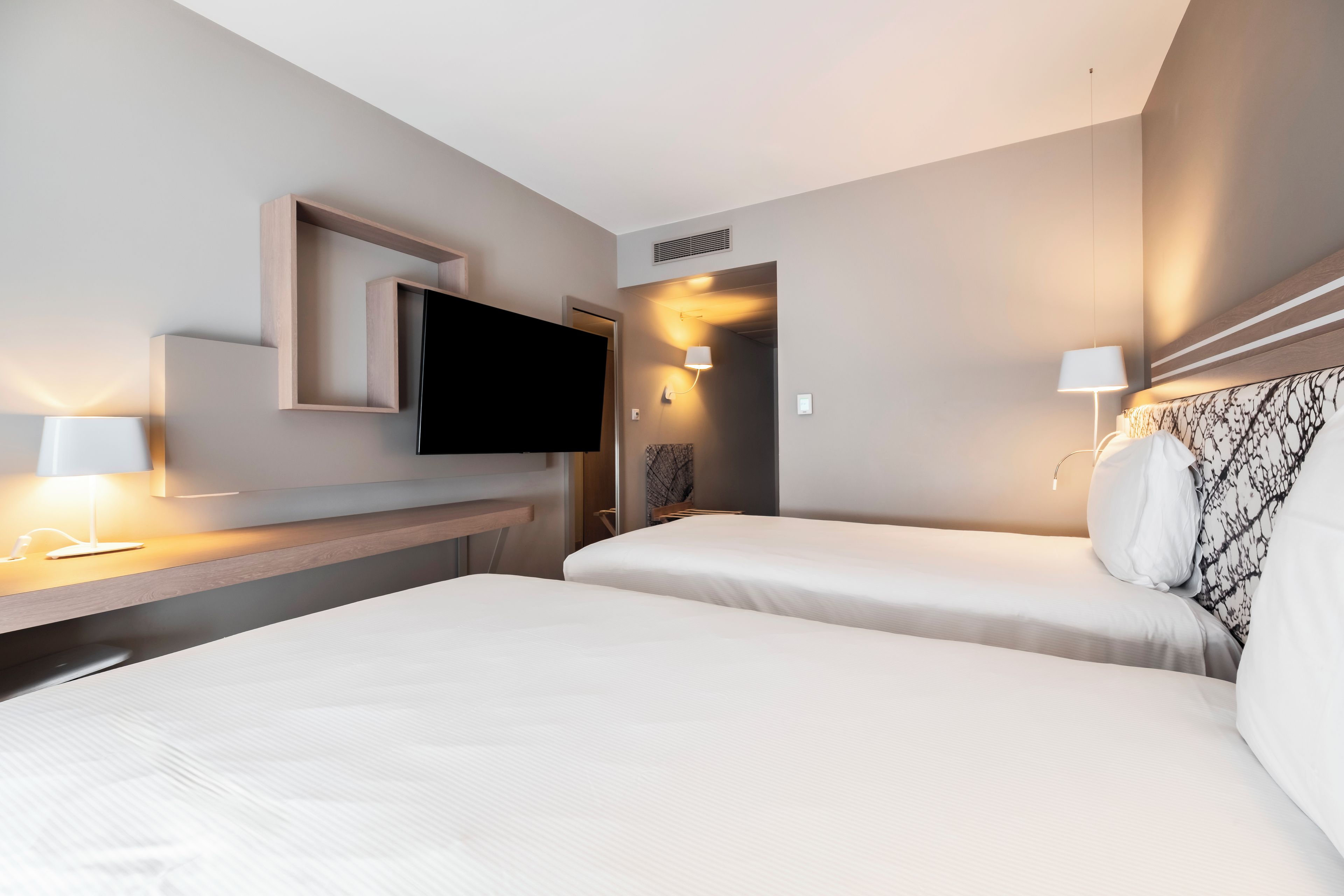 Une chambre d’hôtel avec deux lits, un téléviseur à écran plat, des lampes de chevet et un bureau en bois.