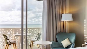 Une chambre d’hôtel avec un lit, une chaise, une table et une vue sur l’océan par une grande fenêtre.
