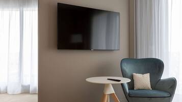 Una sala moderna con un televisor de pantalla plana montado en la pared, una mesa redonda de madera con un control remoto y un sillón azul con cojín.