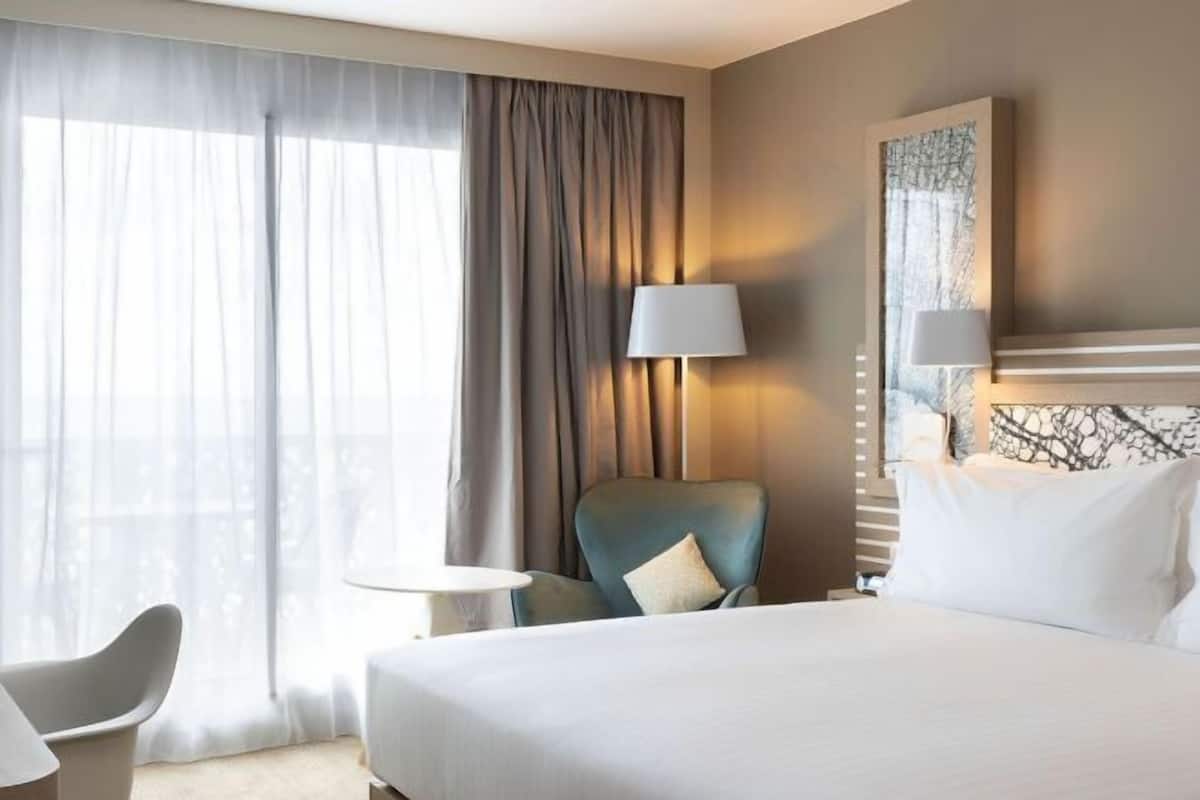Une chambre d’hôtel avec un lit, une chaise, une table, une lampe et un tableau au mur.