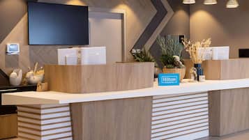 Un mostrador de recepción moderno de hotel con un televisor de pantalla plana, un reloj digital y un cartel de Hilton Honors.