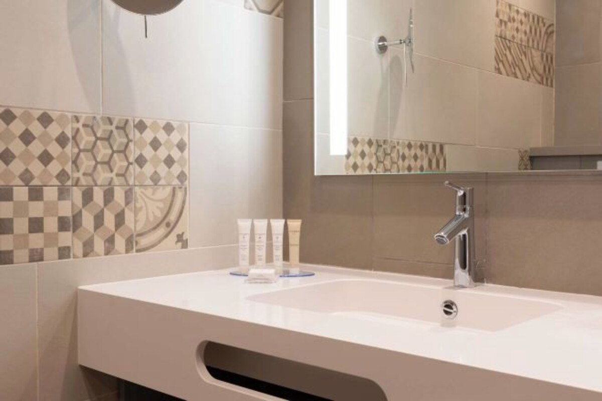 Een moderne badkamer met een wit wastafelmeubel, een spiegel en betegelde wanden.