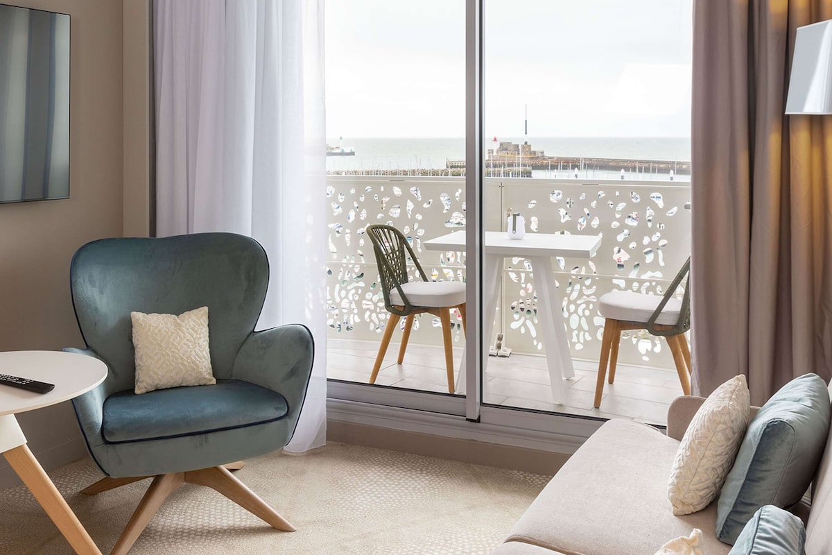 Une chambre d’hôtel moderne dotée d’un balcon, d’un canapé, d’un fauteuil et d’une télévision.