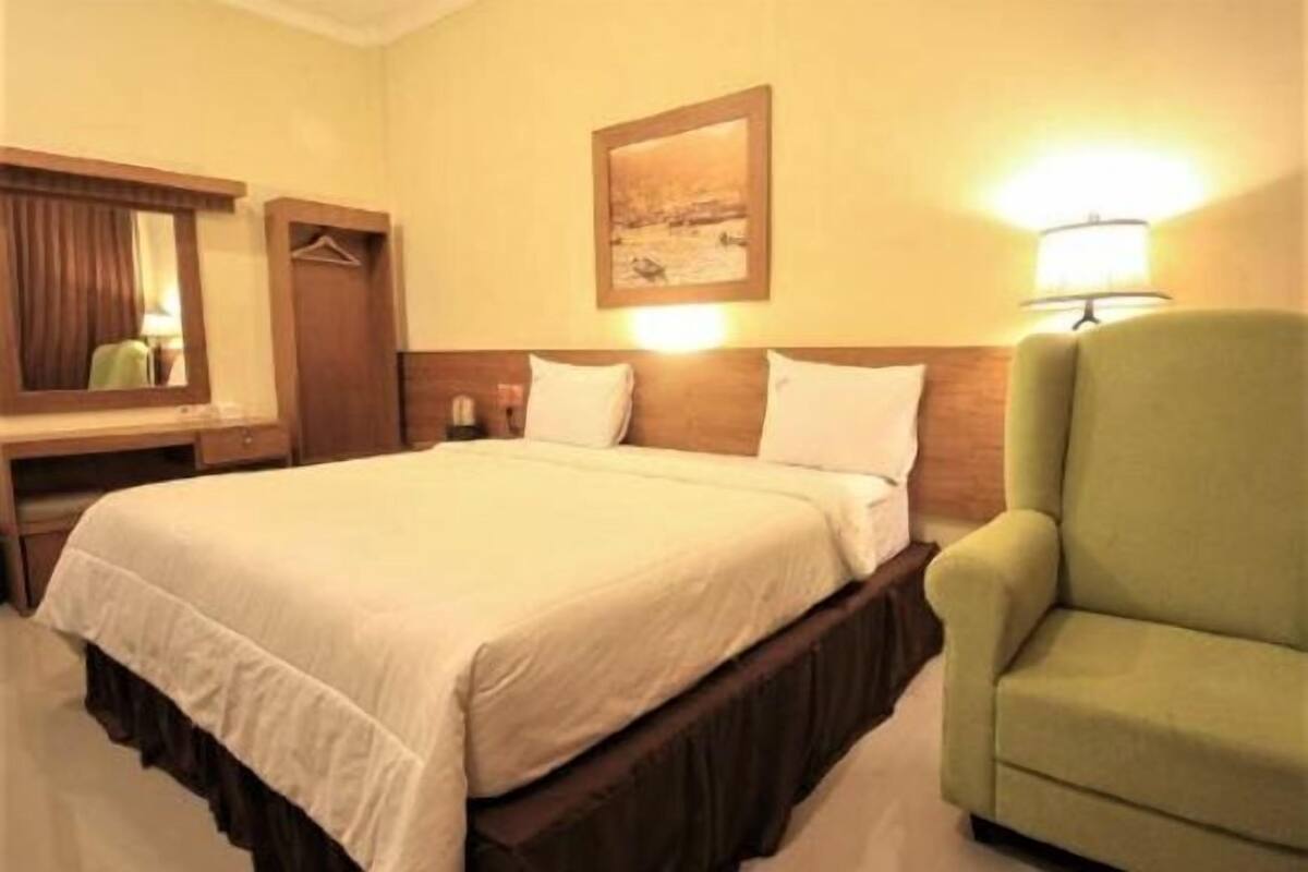 Una habitación de hotel con una cama, una silla, un escritorio, un espejo y un cuadro colgado en la pared.