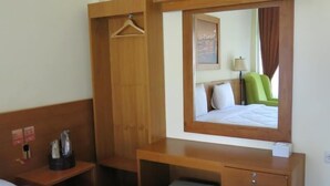 Una habitación de hotel con un escritorio de madera, un espejo, una cama y un taburete pequeño.