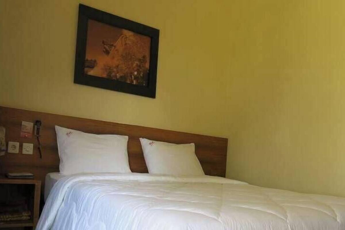 Una cama con ropa blanca, un cabecero de madera y un cuadro en la pared.