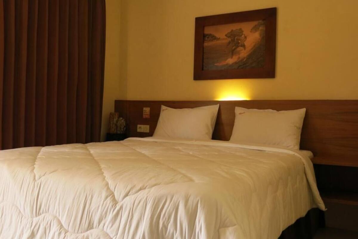 Una habitación de hotel con una cama, una mesita de noche, un cuadro en la pared y una cortina.