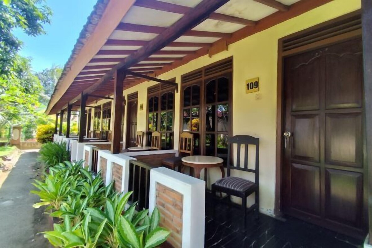 A covered outdoor seating area with tables and chairs, a door marked with the number 109, and a pathway lined with plants.