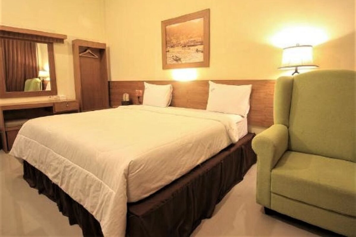 A hotel room with a bed, a desk, a chair, a mirror, a lamp, and a painting on the wall.