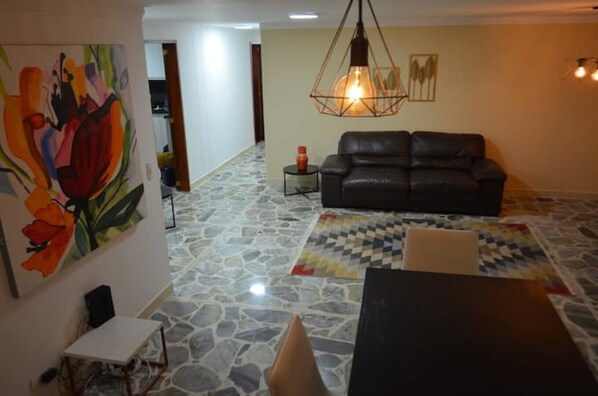 Una sala de estar con piso de piedra, un sofá de cuero negro, una mesa y una lámpara colgante.