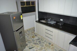Una cocina compacta con refrigerador, pileta y muebles blancos.
