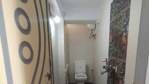 Een smalle badkamer met toilet, douche en wastafel. Links een decoratieve deur en rechts een handdoekhouder aan de muur.