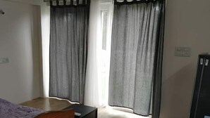 Een kamer met een bed, een klein tafeltje en gordijnen voor de ramen.