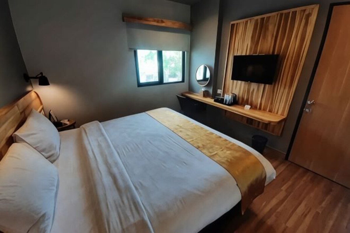 Een slaapkamer met een bed, een aan een houten muur bevestigde televisie, een raam en een spiegel.