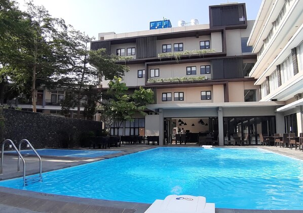 Ein modernes Hotel mit Swimmingpool, Sitzgelegenheiten im Freien und einem überdachten Bereich mit Tischen und Stühlen.