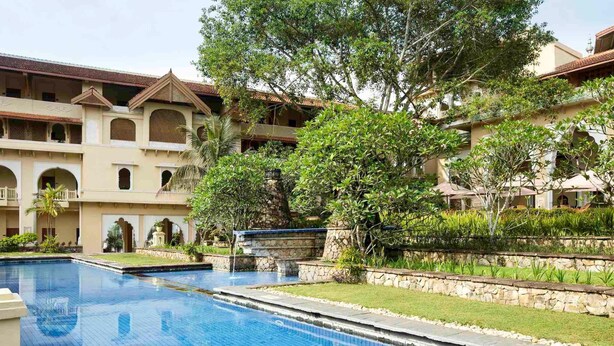 A swimming pool with a stone border, surrounded by a building with multiple balconies and a garden area. - Grand Gallery Bukittinggi (Bukittinggi)