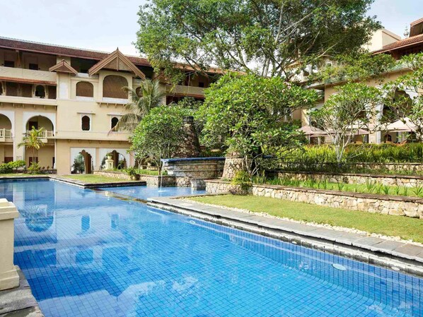 A swimming pool with a stone border, surrounded by a building with multiple balconies and a garden area. - Grand Gallery Bukittinggi (Bukittinggi)