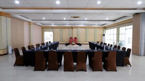 A conference room with a long table, brown chairs, and a stage with a red tablecloth. - Sutan Raja Hotel Kolaka (Kolaka)