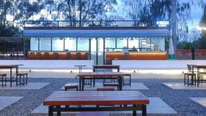 An outdoor seating area with tables and benches, a covered seating area with chairs, and a building with a sign that reads 'D'BRERE CAFE'. - Sutan Raja Hotel Kolaka (Kolaka)