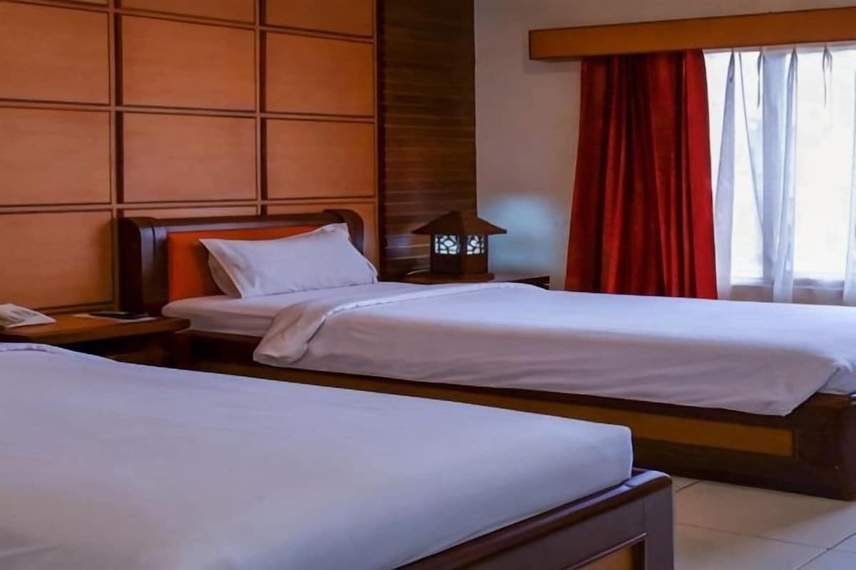 Una habitación de hotel con dos camas individuales, una mesita de noche con lámpara y una ventana con cortinas rojas.