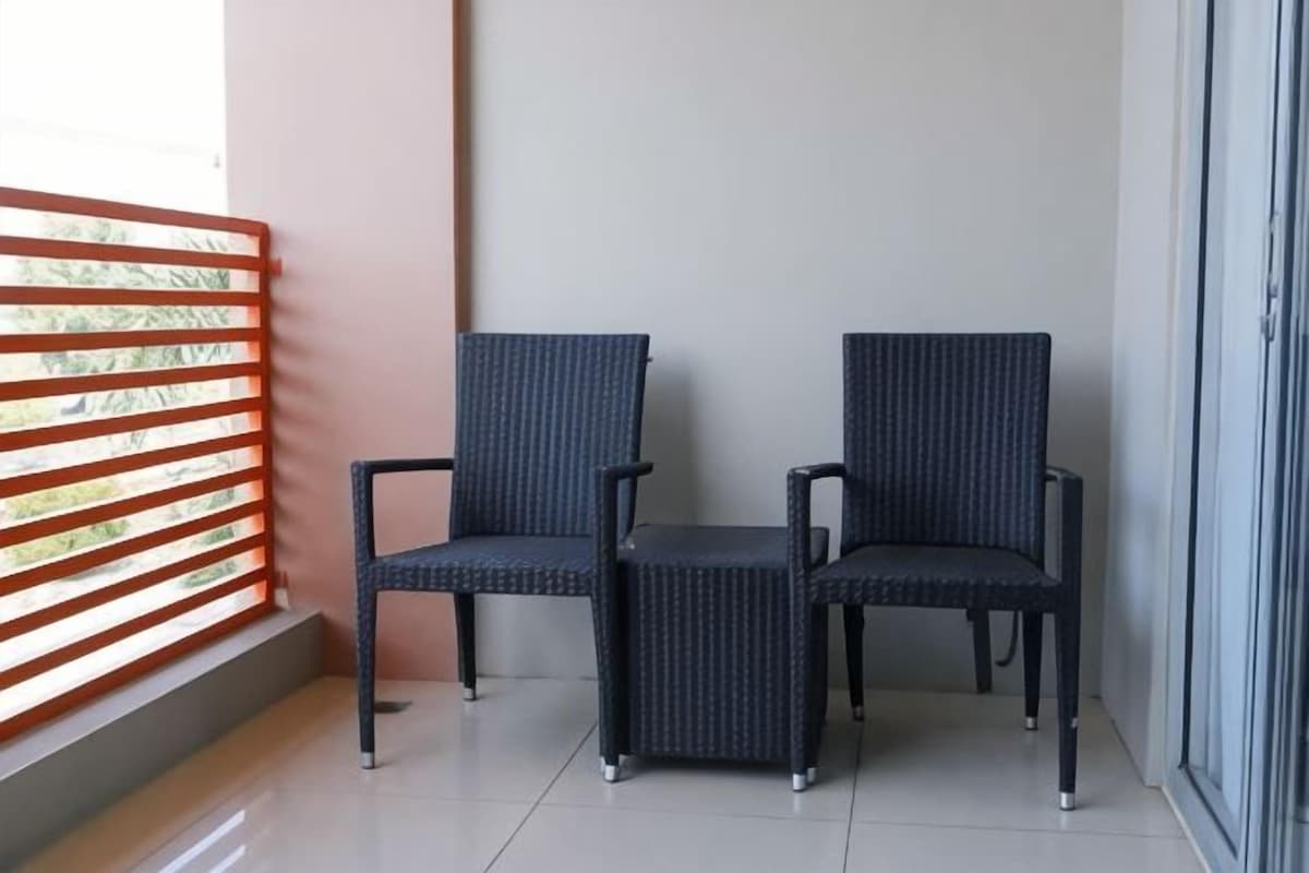 Two chairs and a small table on a balcony with a metal railing and a glass door.