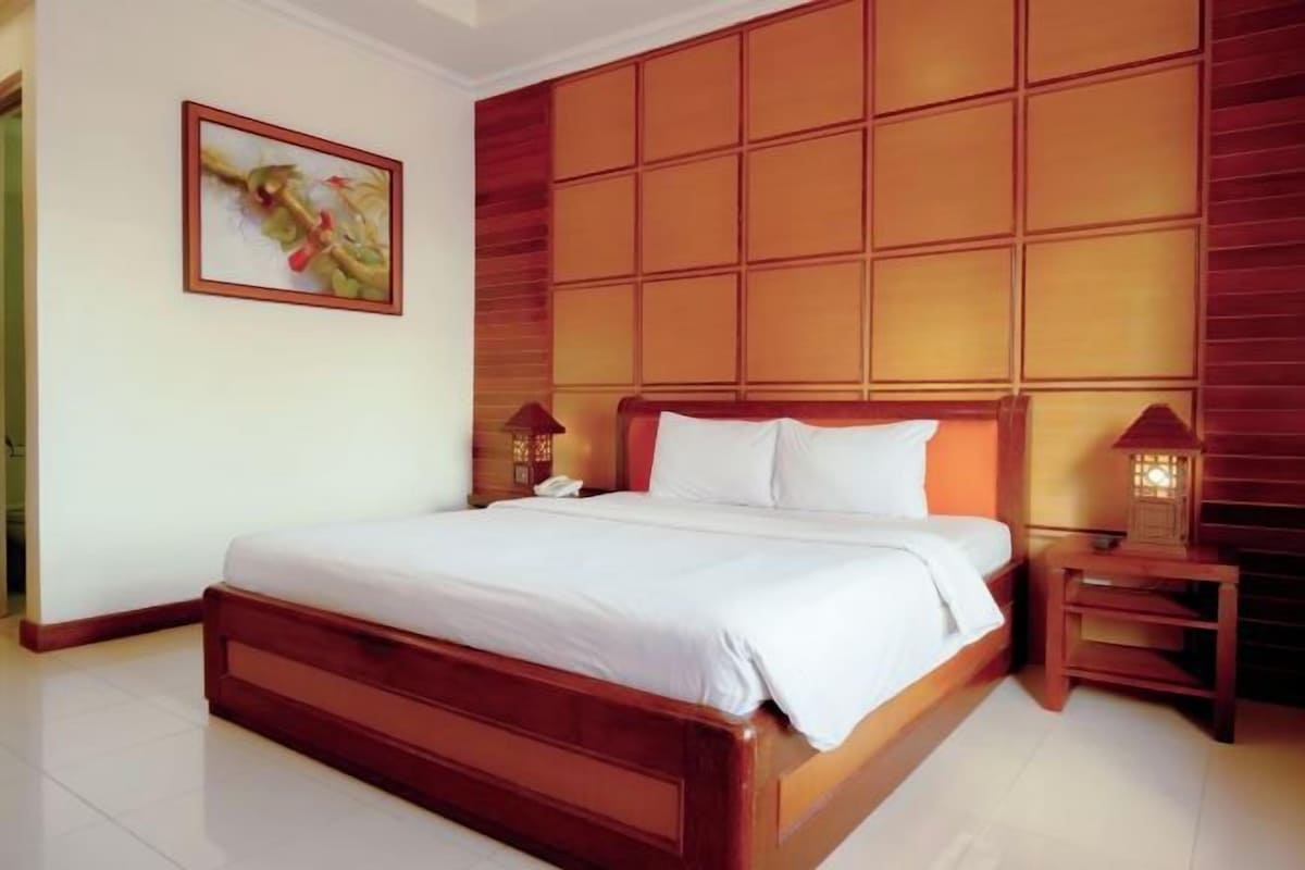 Habitación de hotel con una cama de madera, una mesita de noche con lámpara y un diseño de panel en la pared.