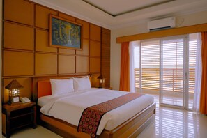 A hotel room with a large bed, a painting above the headboard, a nightstand with a lamp, and a window with blinds. - Sutan Raja Hotel Kolaka (Kolaka)