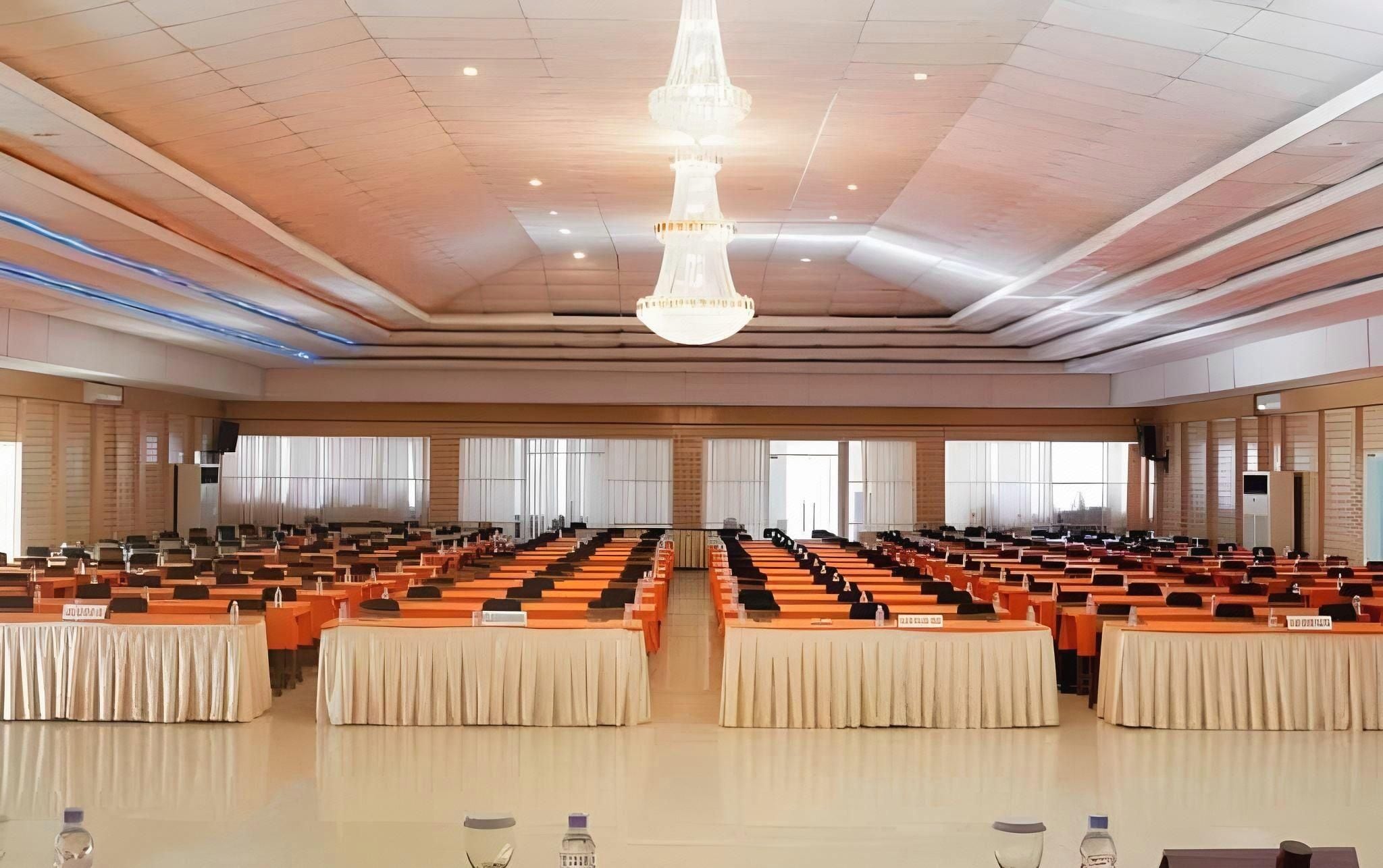 A large conference room with rows of tables and chairs, a chandelier, and large windows.
